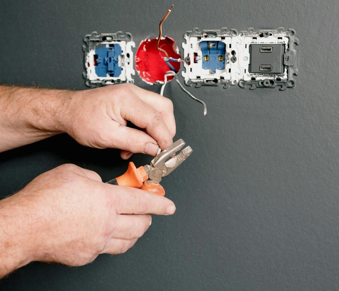 Crop faceless electrician using pliers for installation sockets and switches in new apartment